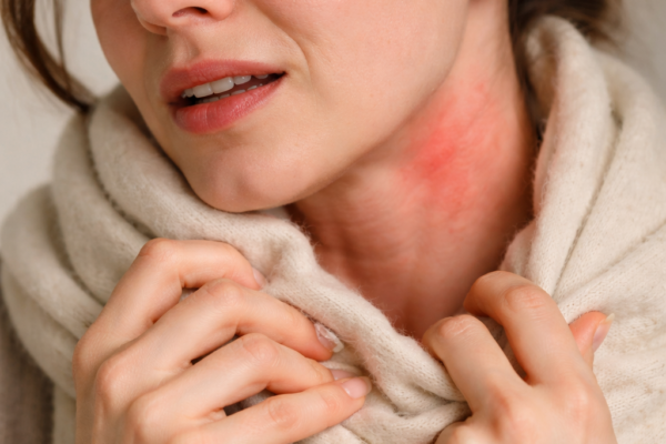A close-up of a person’s face with a pained expression as they pull a soft scarf away from their neck, symbolizing skin sensitivity and anxiety.