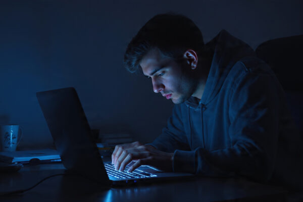 young adult sitting hunched over a laptop in a dark room