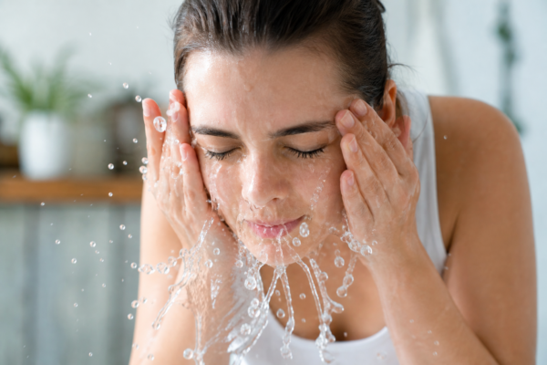A person washing their face with cool water to soothe skin irritation and burning.